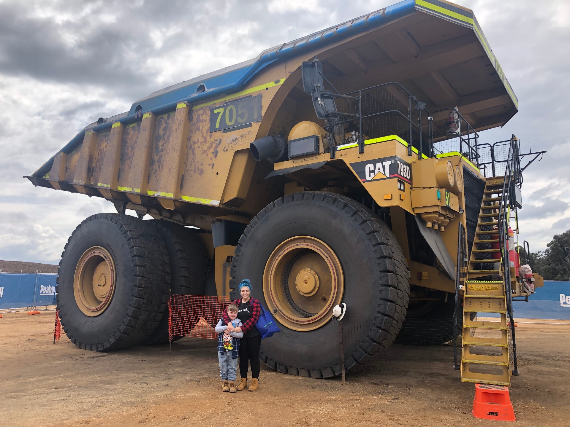 Carly, founder of Grit to Glow Skin Co, with her son in front of a CAT 793D haul truck